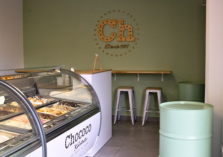 Imagen del interior de uno de los establecimientos de Chococó en la que se muestra una vitrina para helados artesanales y al fondo una mesa con taburetes
