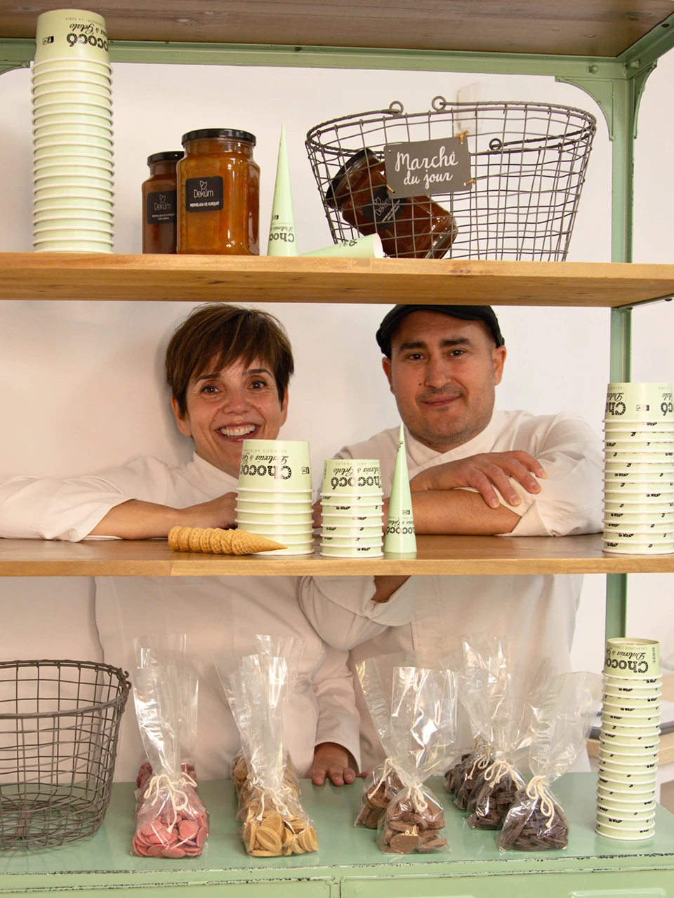 Imagen de José y Lorena gerentes de Chococó detrás de una estantería con utensilios y productos de heladería mientras miran muy sonrientes a la cámara